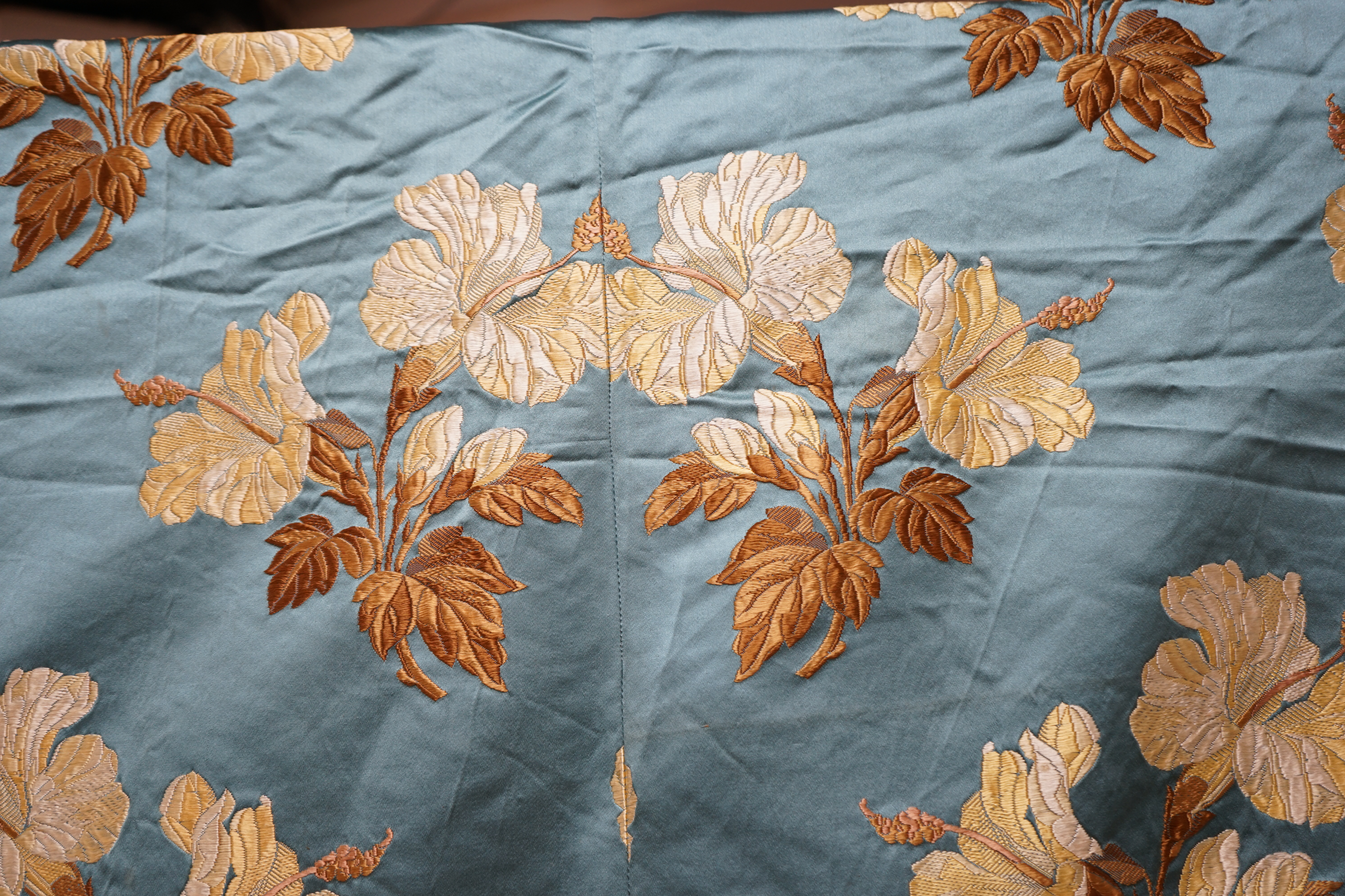 A turquoise satin floral silk brocaded panel of four 59cm widths, boldly embroidered in yellow and brown strays of lilies, the panel possibly part of a pelmet or half tester bed, each spray being 21cm high as a diagonal